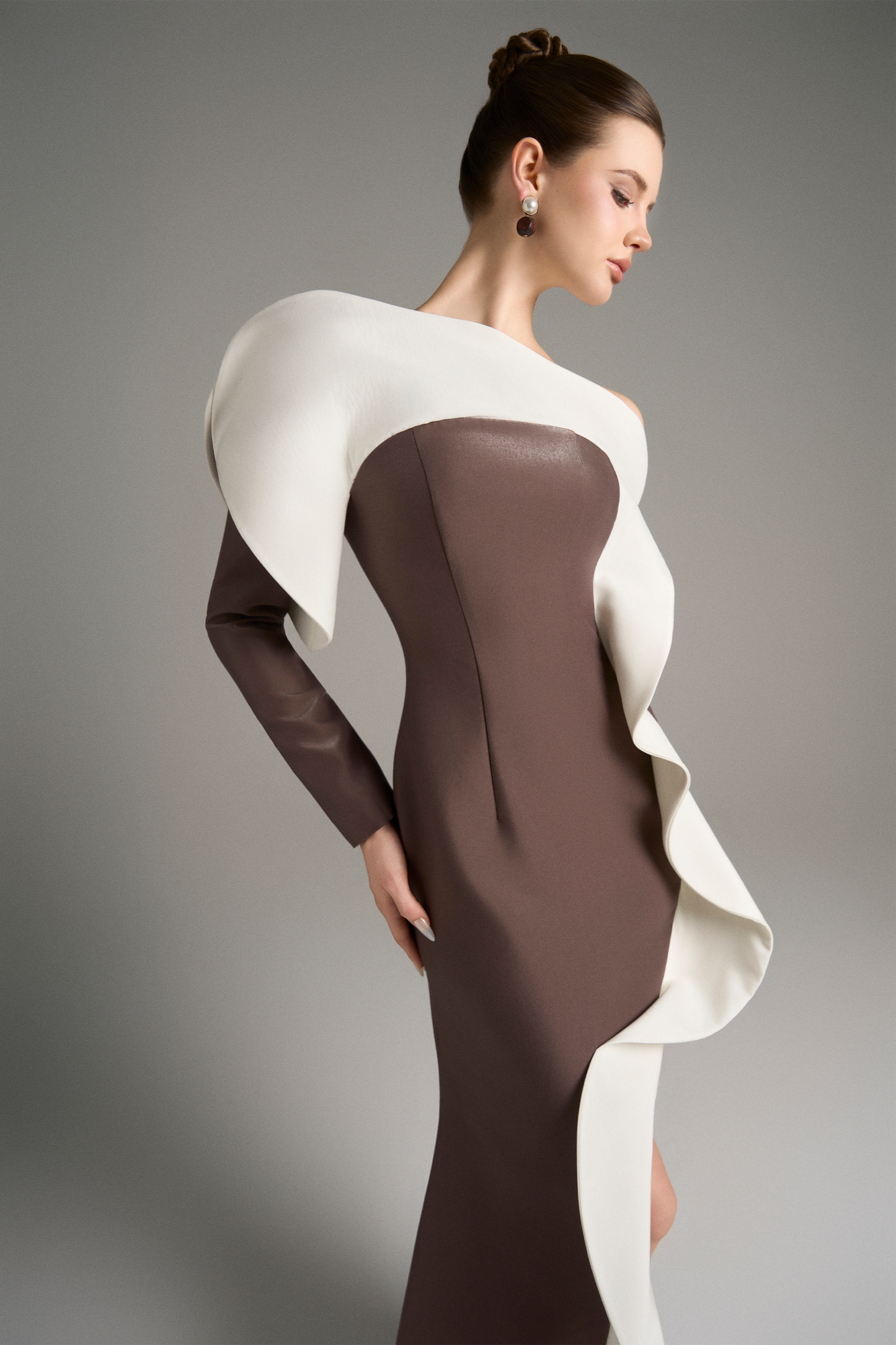 Side angle of the model in the brown gown, highlighting the voluminous white ruffle that spirals from the shoulder to the slit.