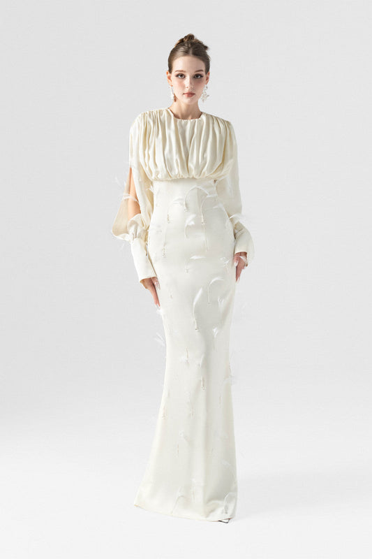 A beige silk maxi dress, adorned with intricate embellishments of feathers, pearls, and crystals.
