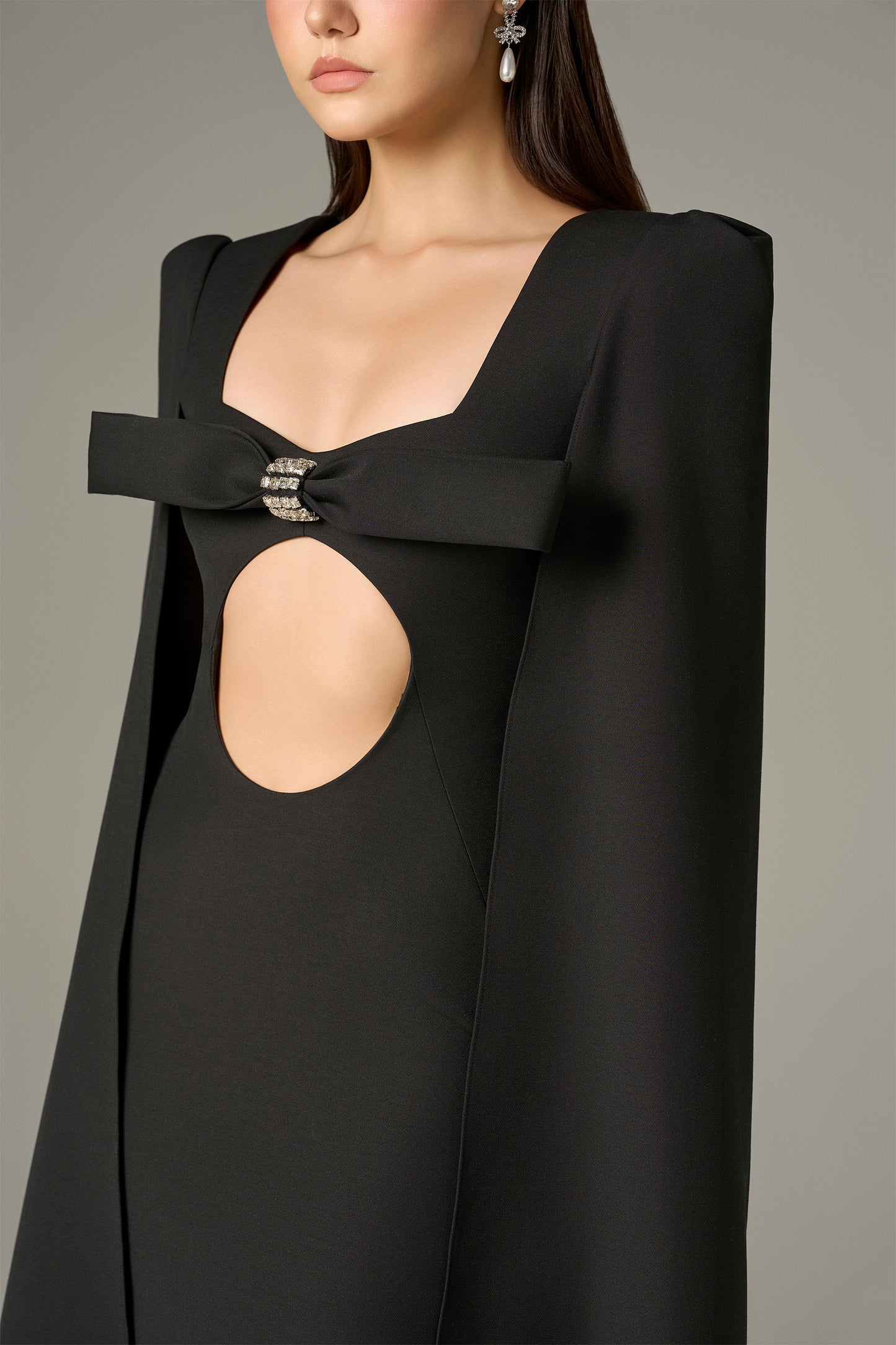 The Black Maxi Dress stuns with a crystal-embellished bow, bold circular cutout and flowing cape sleeves.