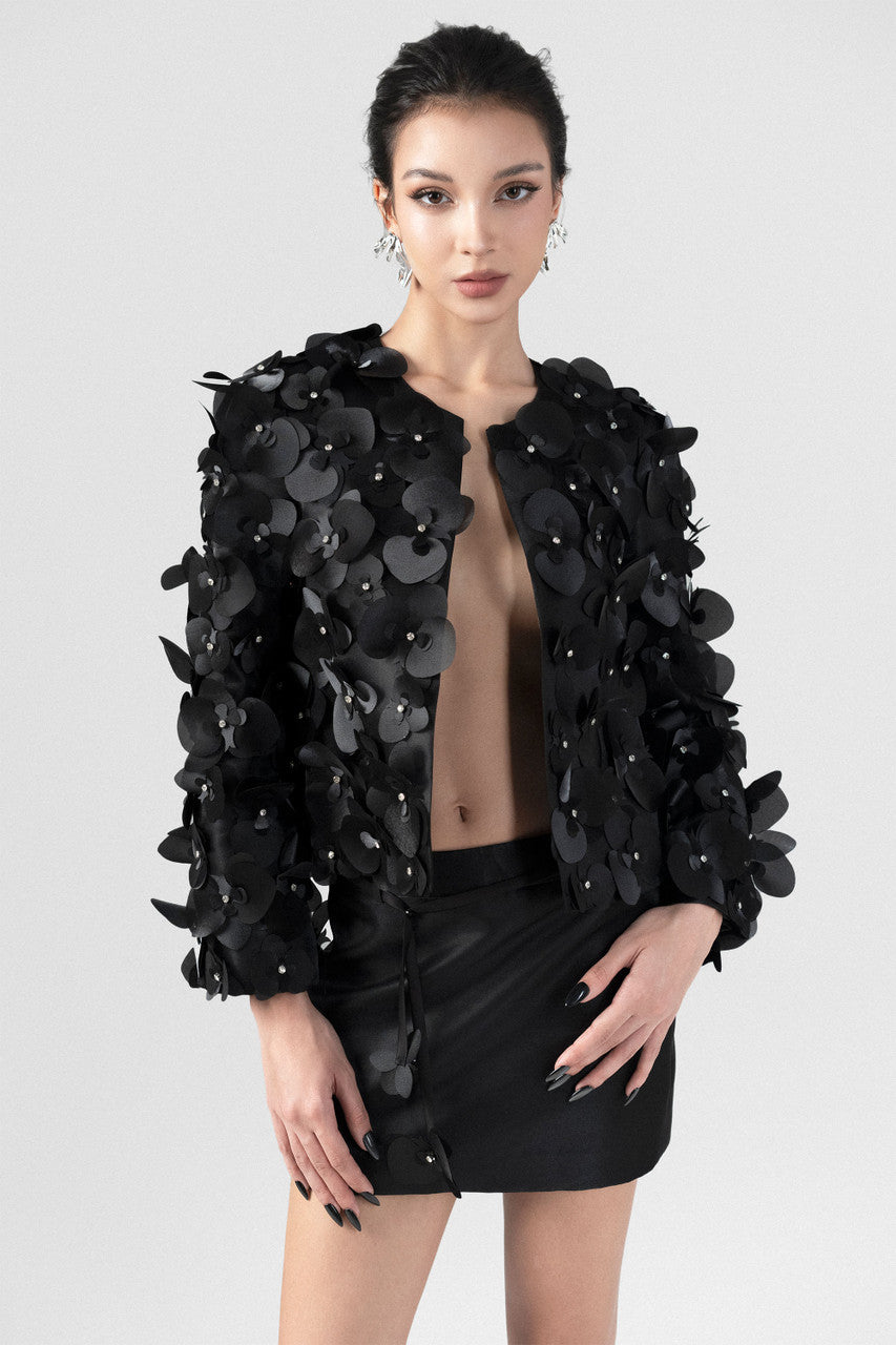 Cropped black jacket in satin, with long sleeves and orchid embellishments.