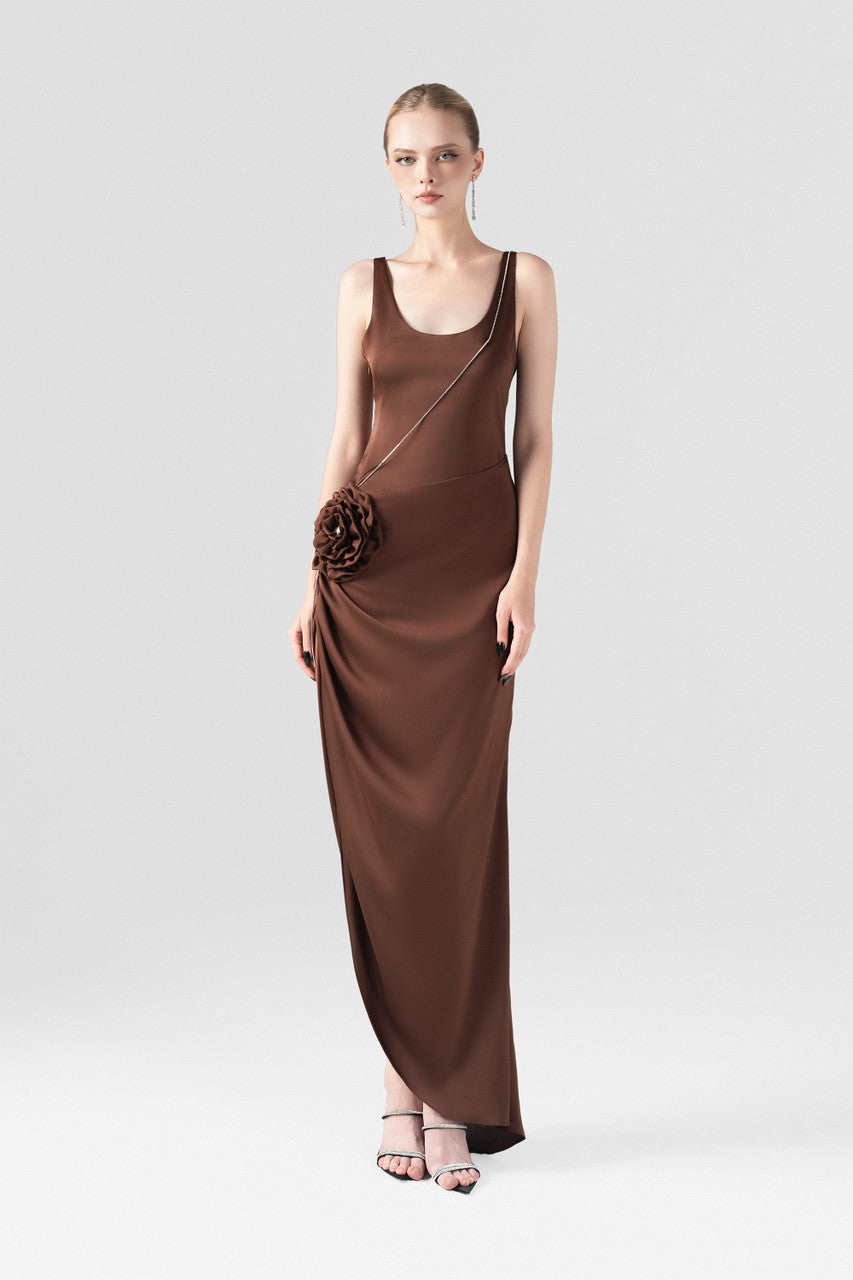 The brown silk maxi dress, detailed with a scoop neckline, hand-sewn rose accent, and stone chain embellishments.