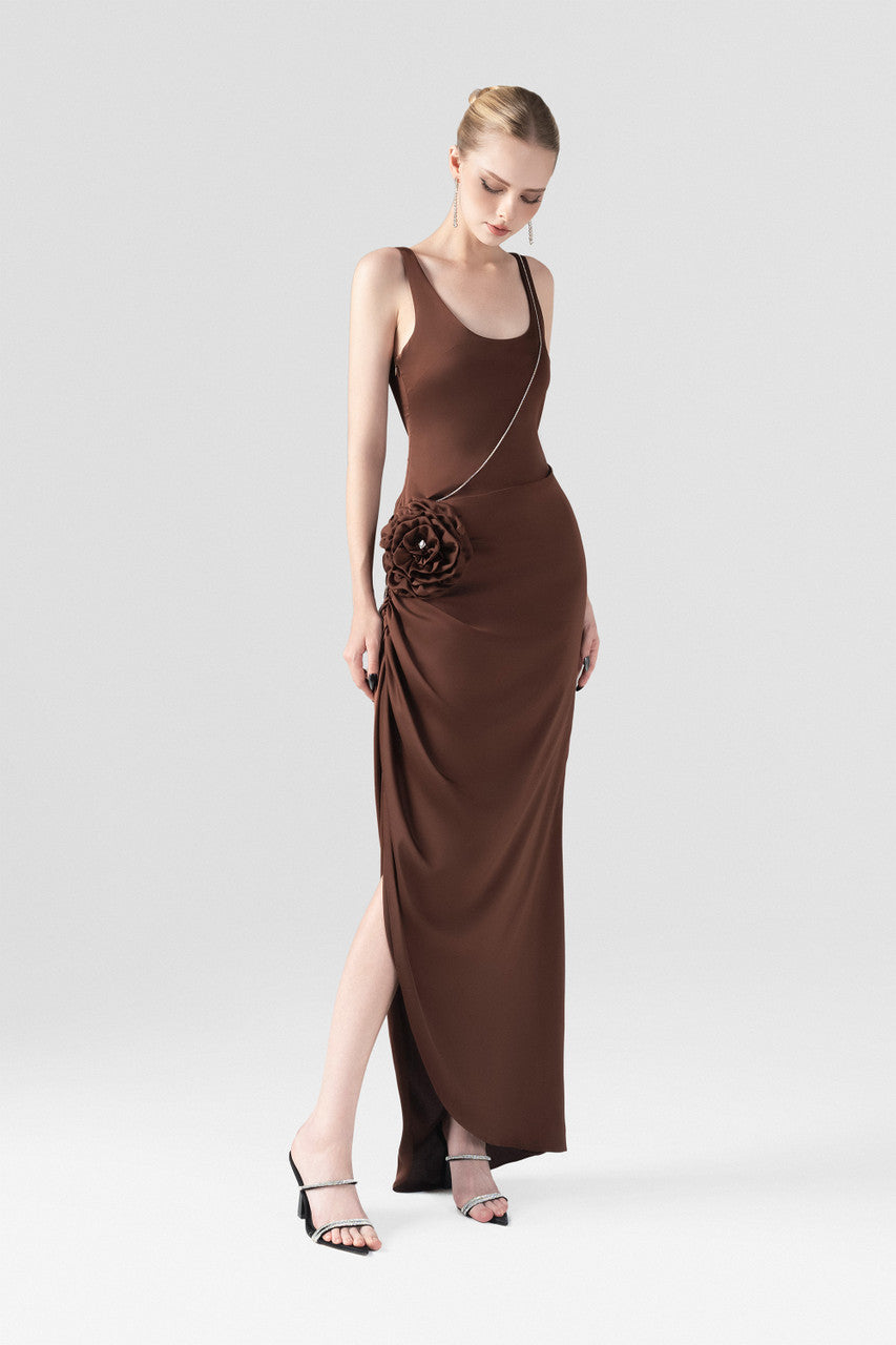 The brown silk maxi dress, detailed with a scoop neckline, hand-sewn rose accent, and stone chain embellishments.