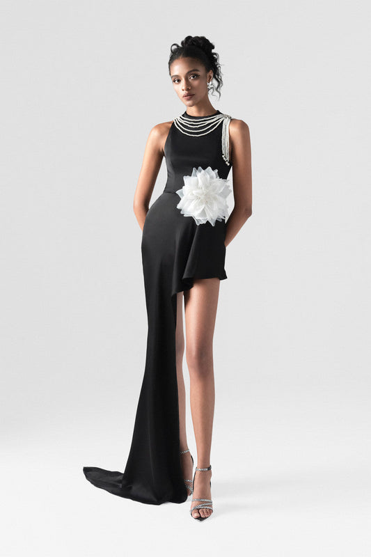 A black silk dress adorned with a white floral accent at the waist, a pearl-detailed neckline, and a long hemline.