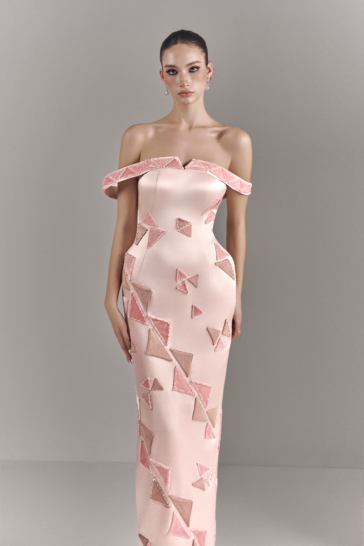 Model wearing a pink off-shoulder dress with geometric pattern against a gray background