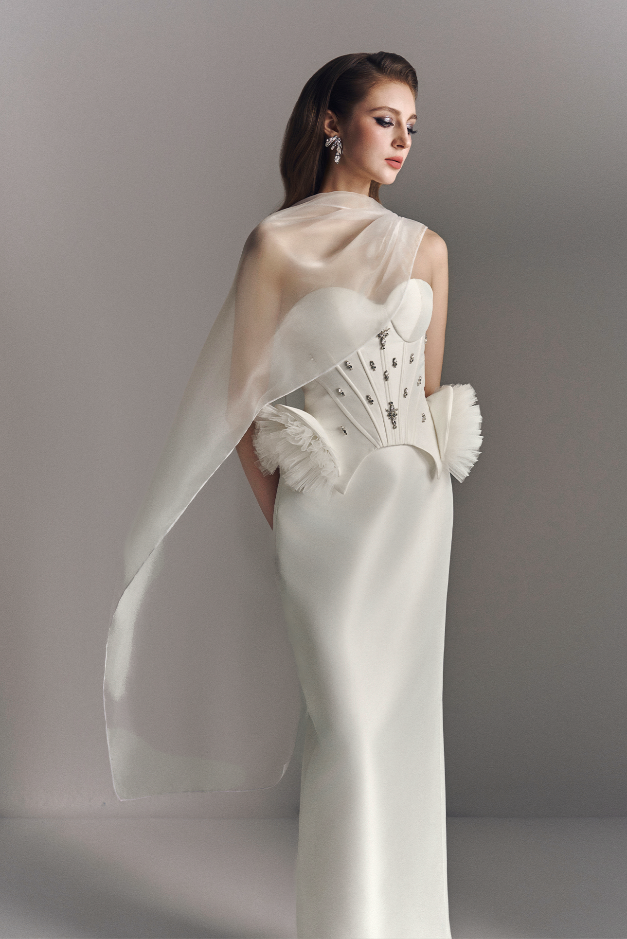 Woman wearing a white wedding dress with a sheer overlay against a gray background