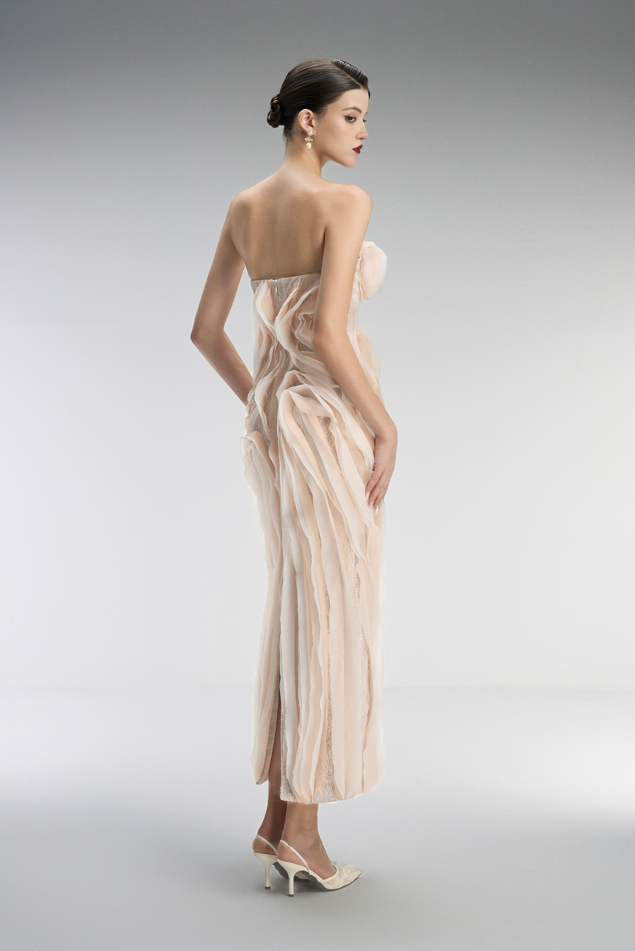 Woman wearing a strapless, long, beige dress against a gray background