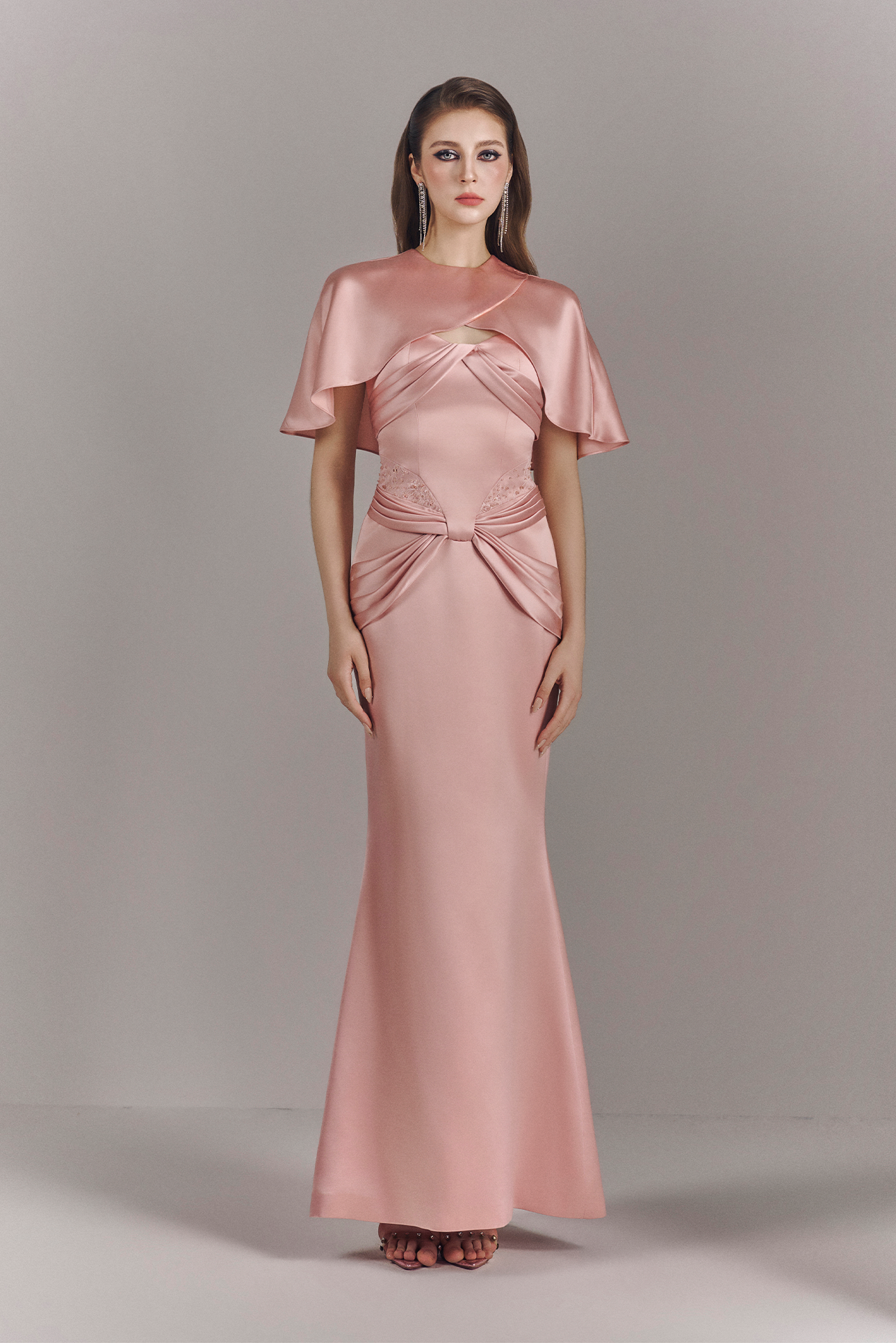 Woman wearing a pink evening gown with cape on a gray background