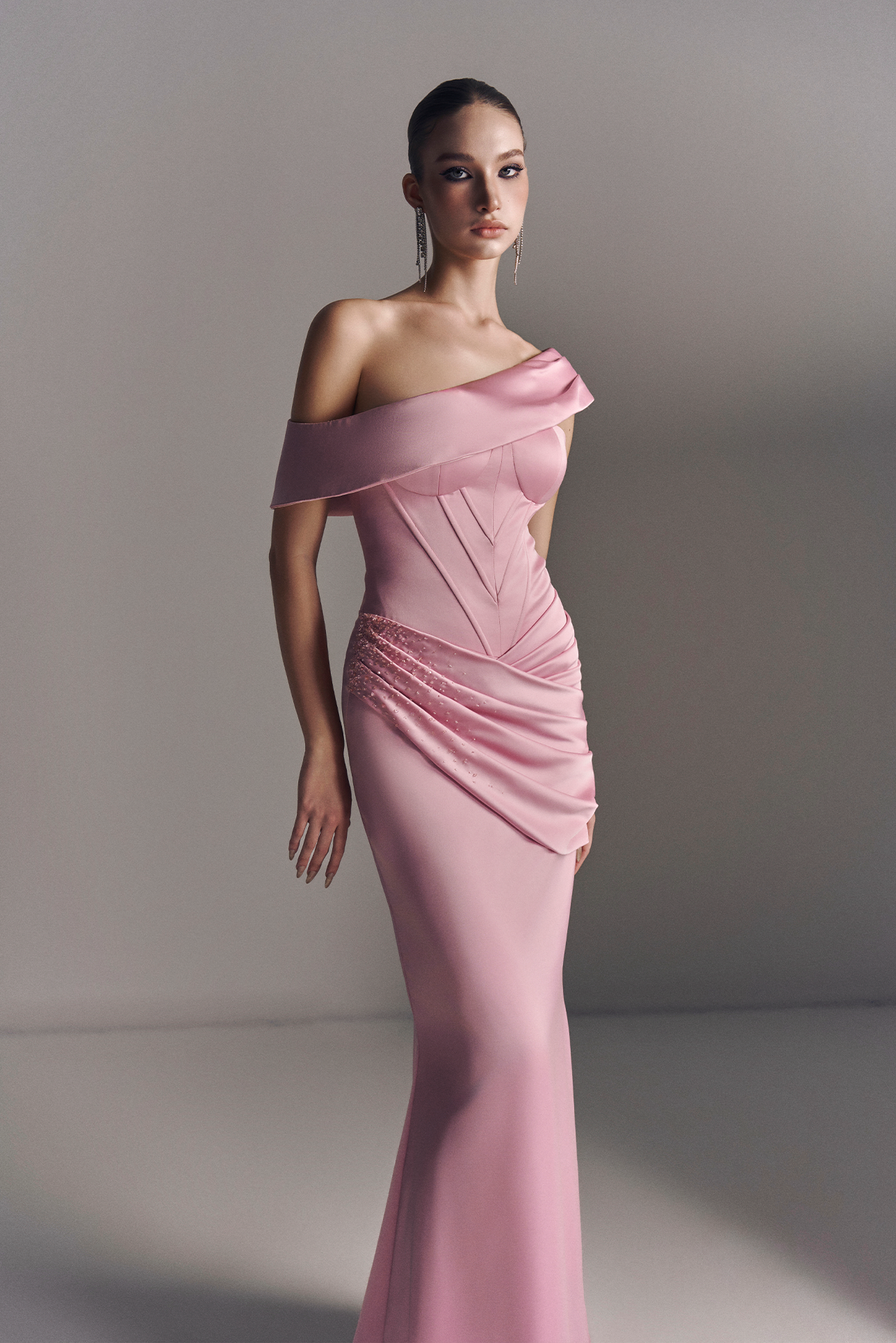 Woman wearing a pink off-shoulder evening gown against a plain background