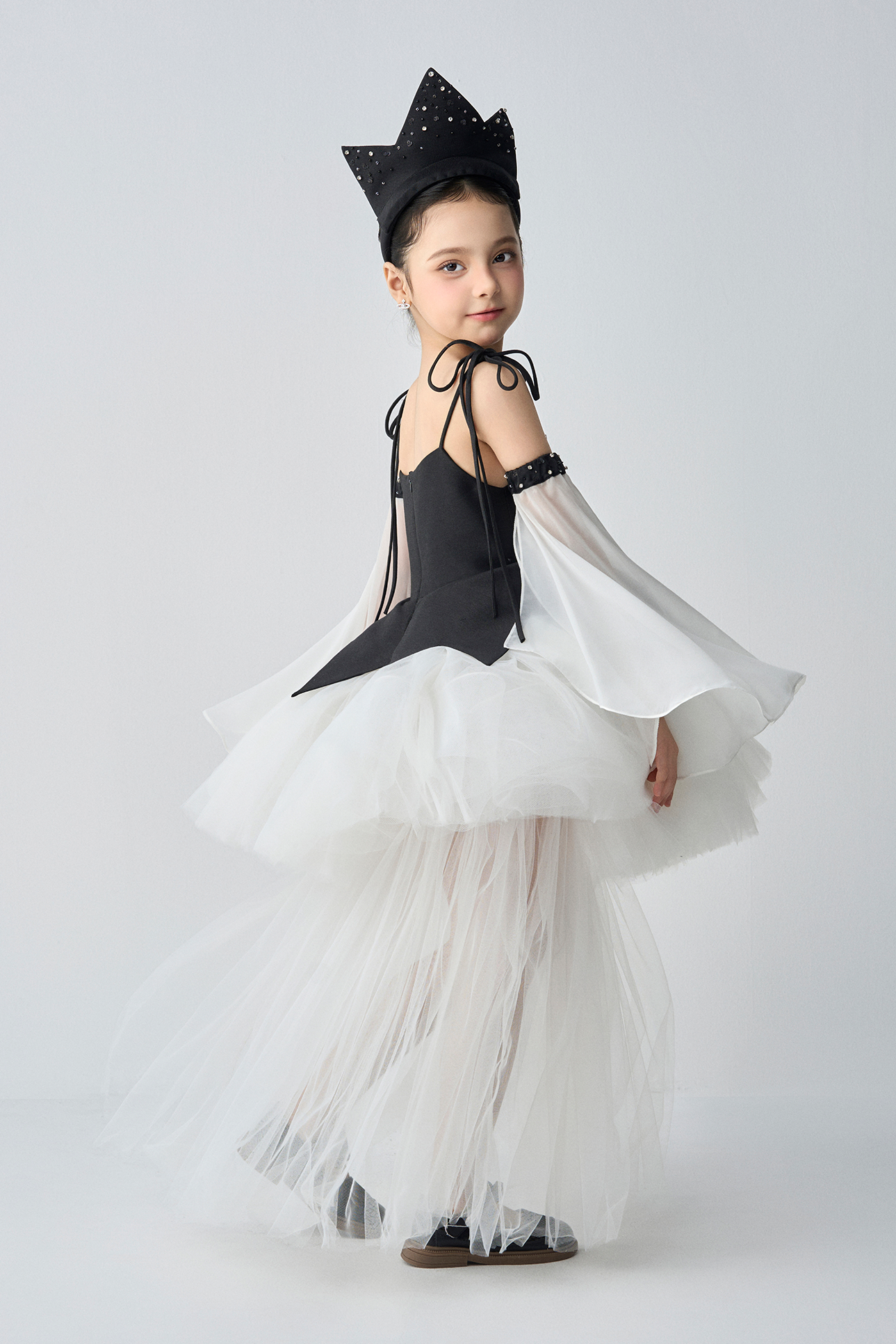 Young girl in a black and white costume with a crown on a white background
