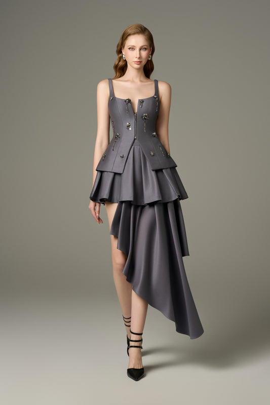 A full-length front view of a Lure grey stone embellished corset top and asymmetrical mini dress set, highlighting the deep V-neckline, handcrafted stone and bead embellishments on the corset, and the multi-layered, asymmetrical hem of the skirt.
