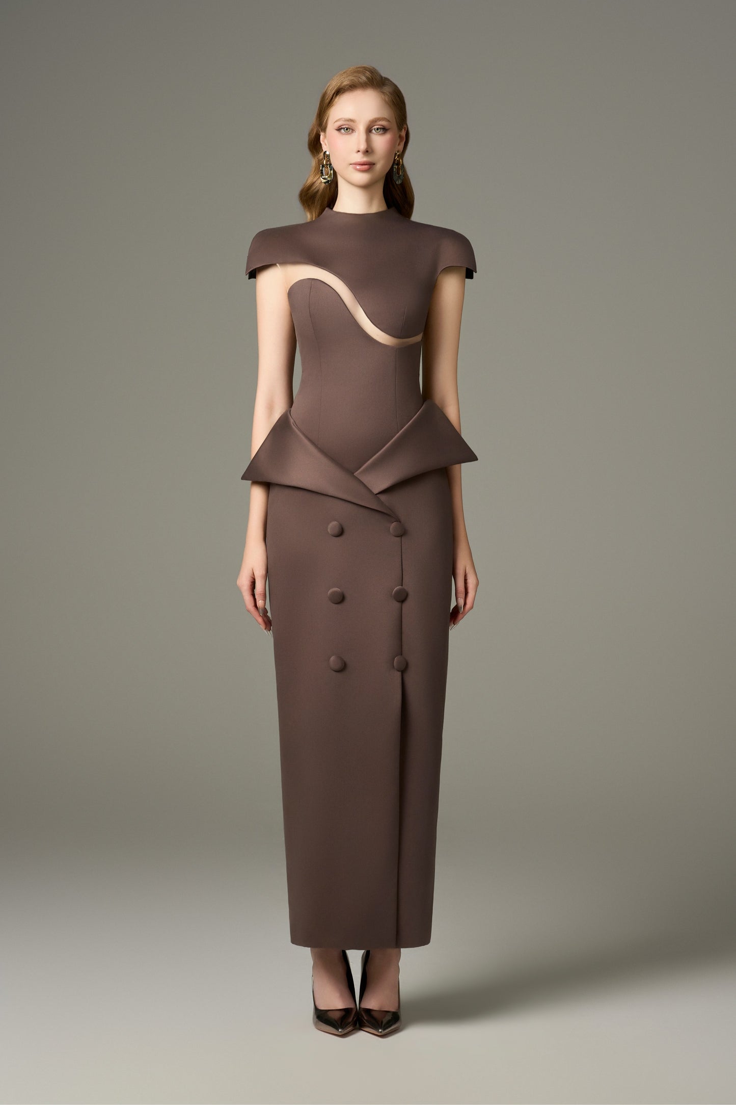 A full-length front view of a Vogue brown short sleeve wave cut-out maxi dress, featuring a figure-hugging fit, round neckline, tailored shoulders with short sleeves, a wave cut-out detail on the bodice, and a peplum detail at the waist over a straight skirt with buttons and a front slit.