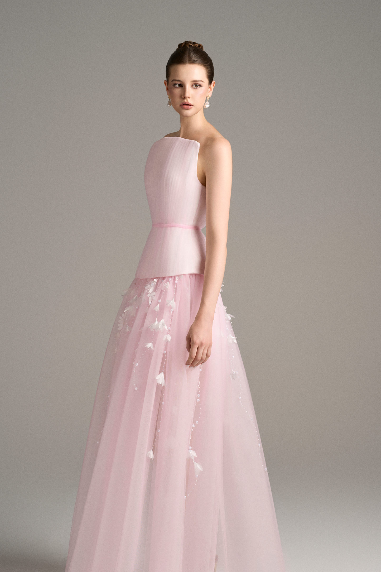 Side angled view of Aveta pastel pink evening gown set showing bandeau corset bodice and sheer layered skirt with cascading floral appliqué accents.