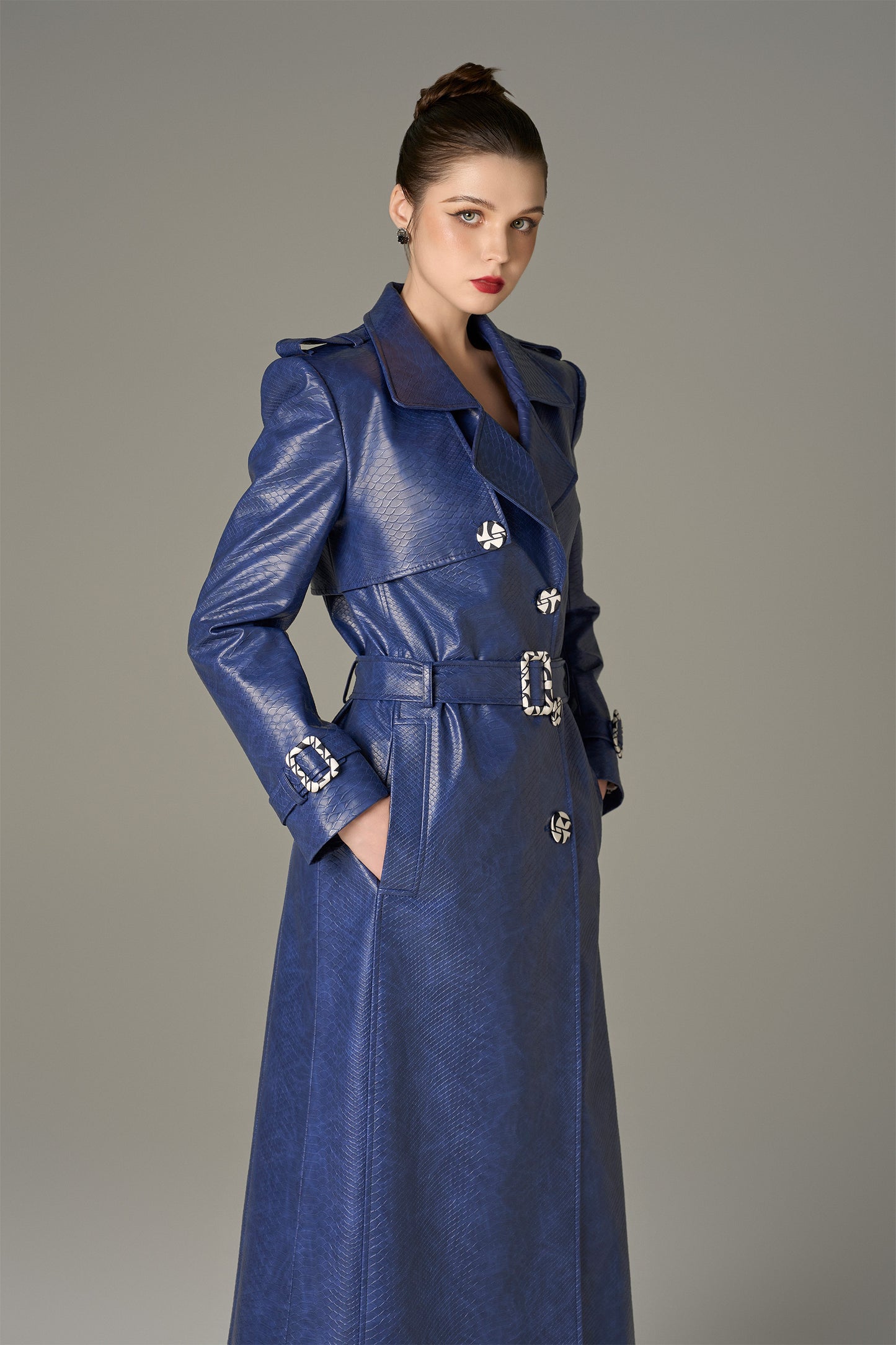 A long coat in navy crocodile-patterned leather, featuring a belt.