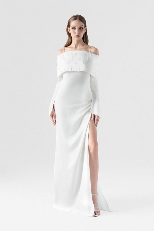 White maxi dress in silk with off-shoulder design, crystal embellishments, and a high side slit with pleating.