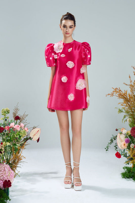 Pink mini dress in organza with A-line shape, puffed sleeves, and floral embellishments.