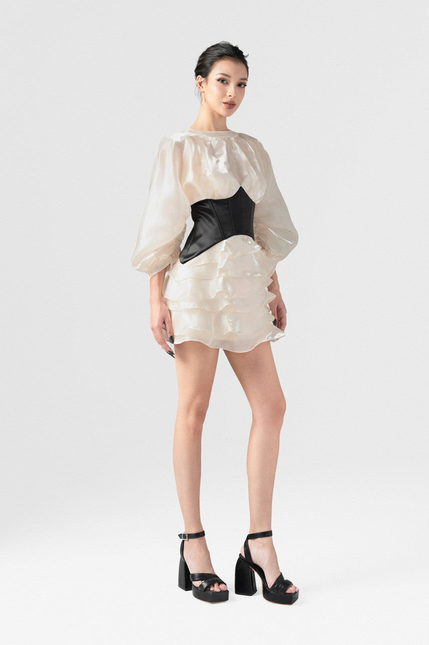 The beige mini dress in silk organza, with long puff sleeves, open back, black corset detailing, and a voluminous skirt.
