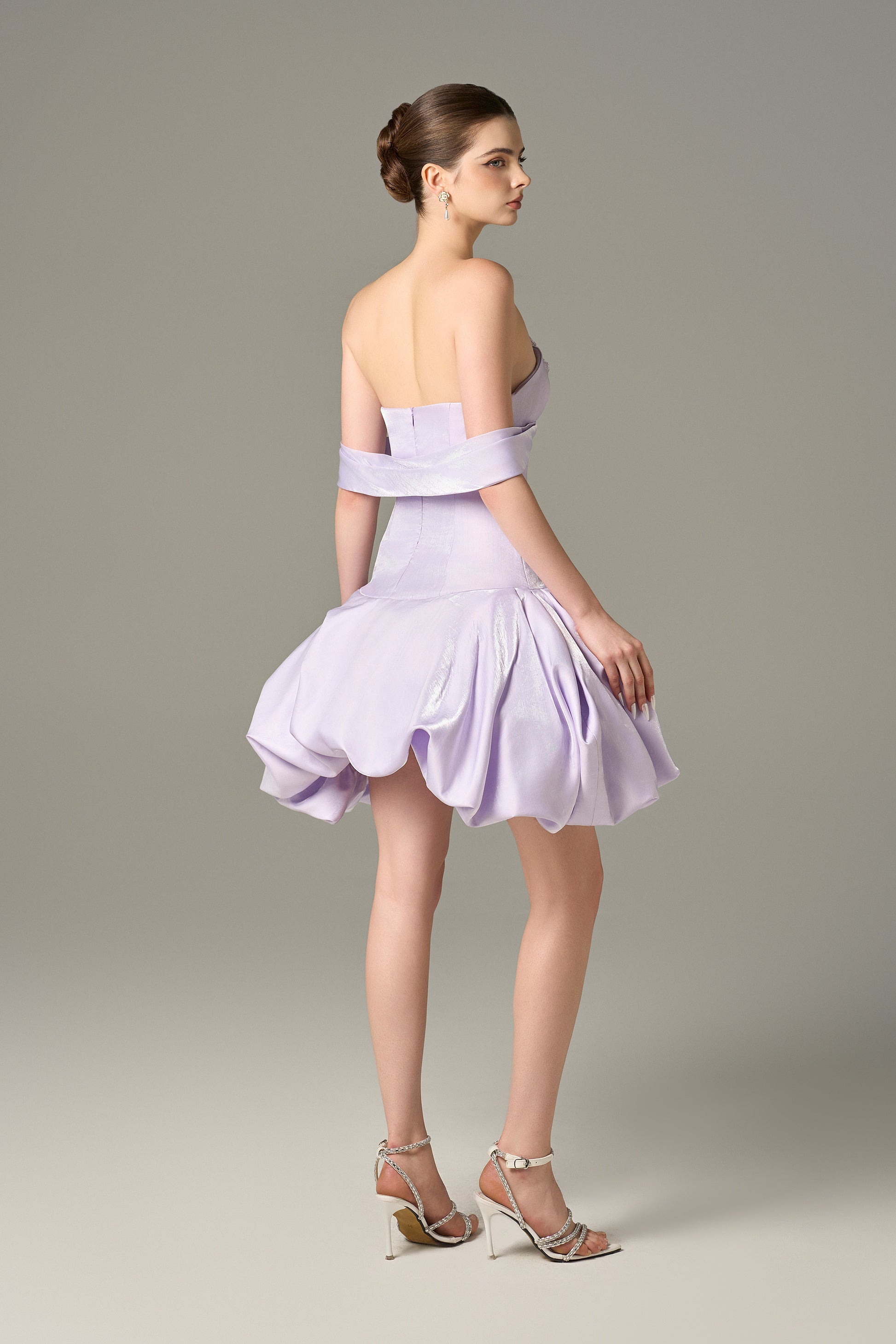 The fitted bodice, crafted in a lavender purple, features a beautifully off-shoulder draped straps.