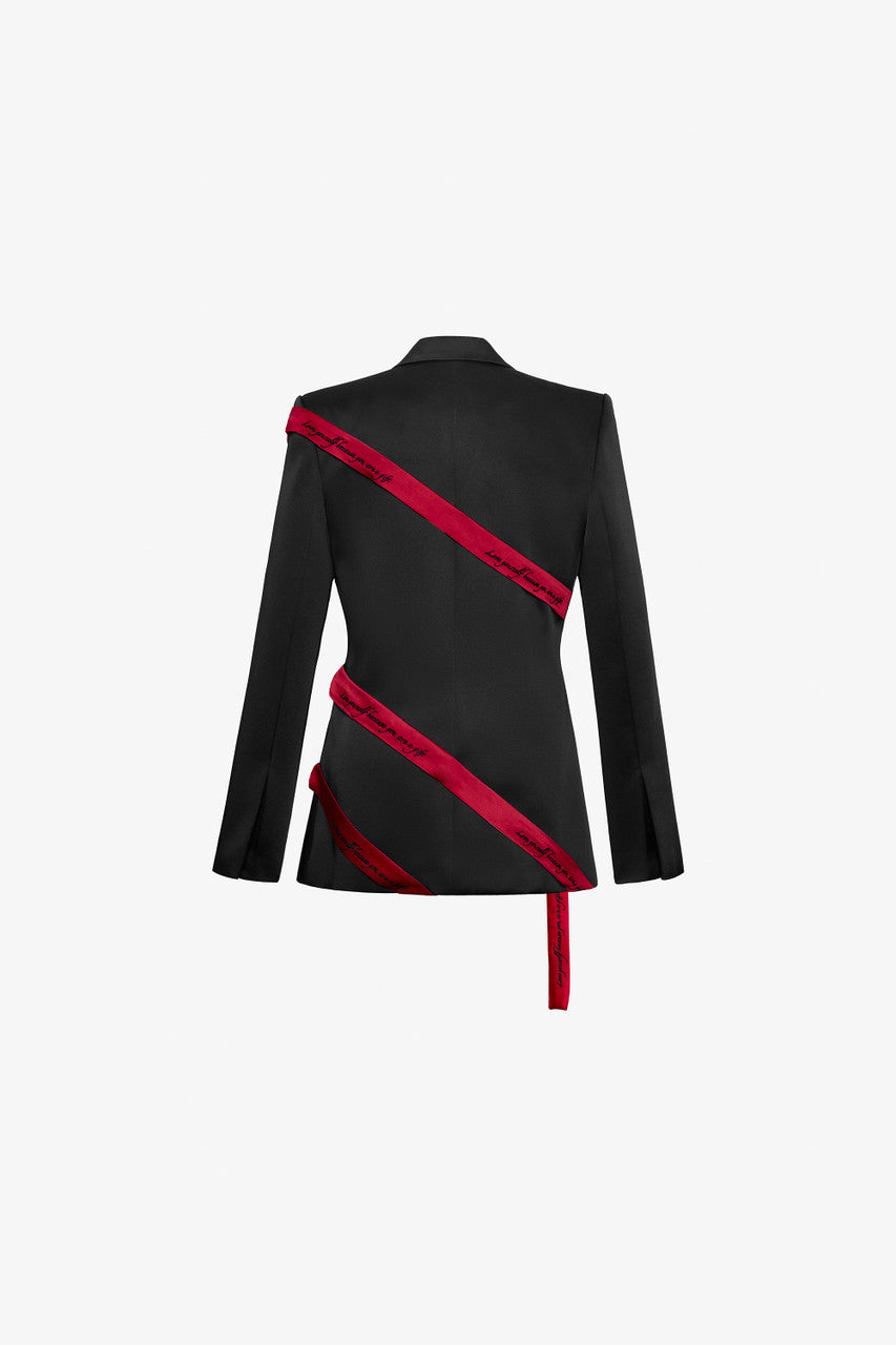 The black blazer in taffeta, featuring diagonal flaps, structured padded shoulders, and red straps