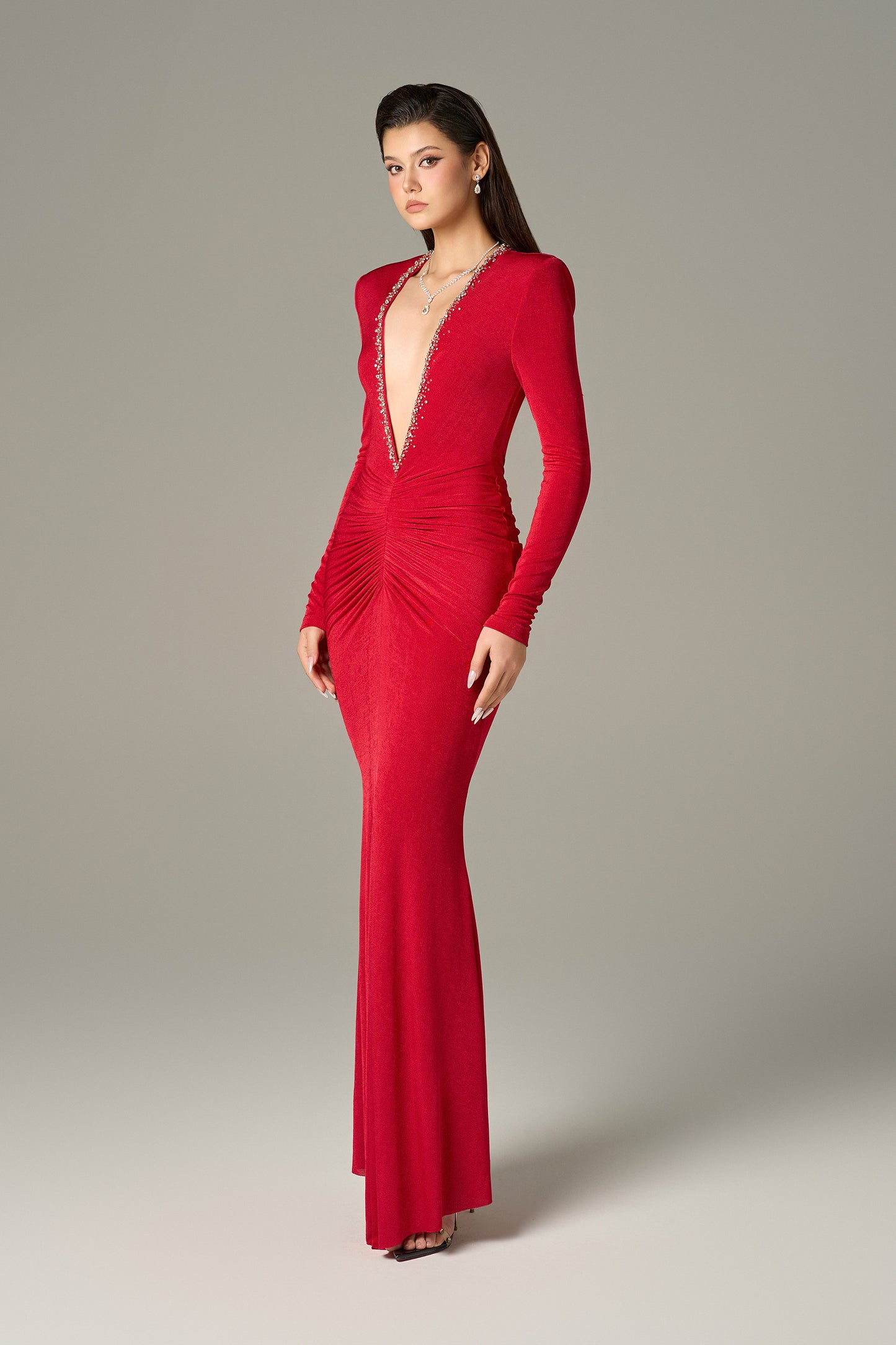 The red maxi dress in spandex, featuring a deep V-neckline with embellished crystals and ruching on both sides.