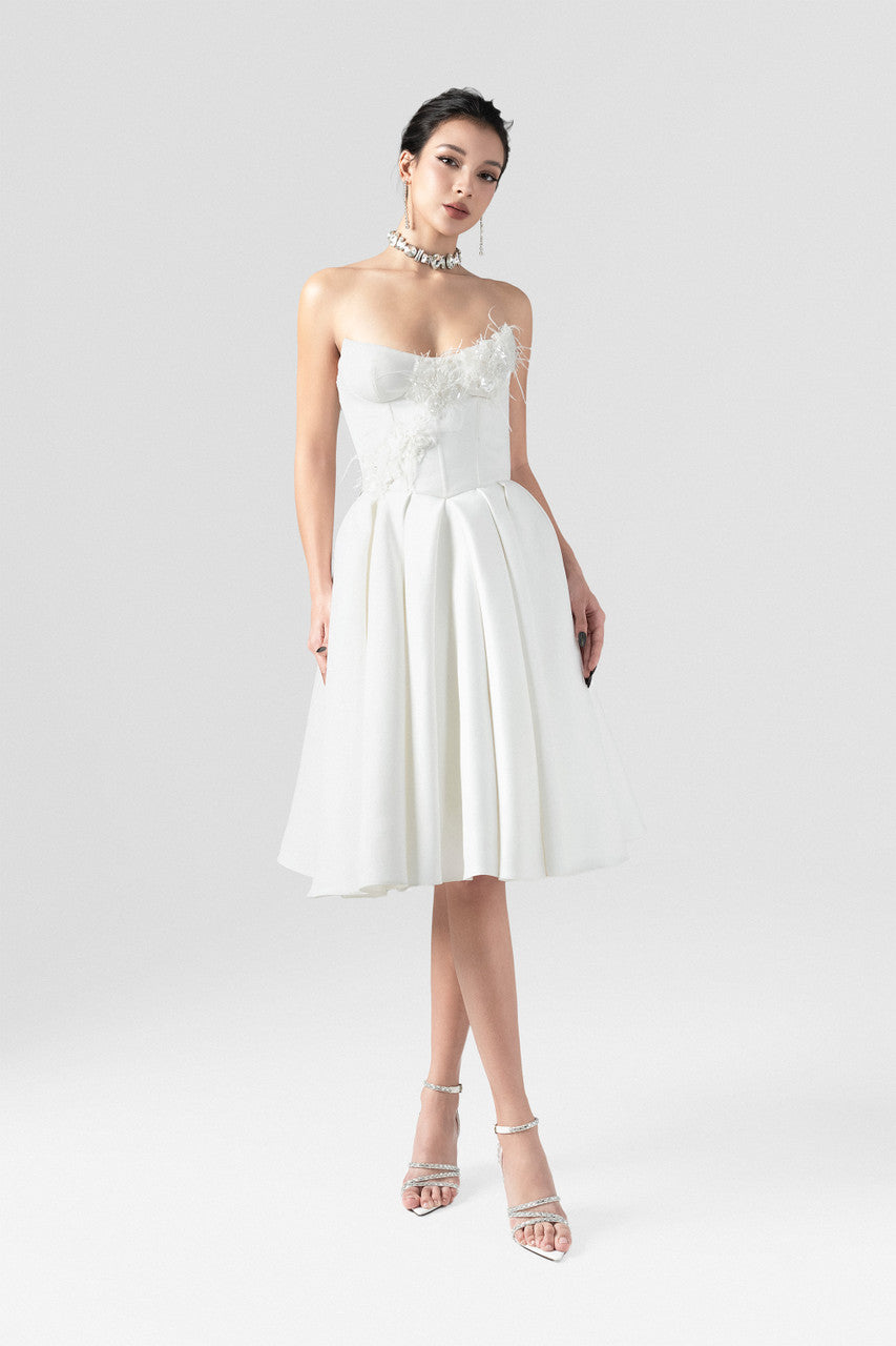 An elegant white midi dress in luxurious taffeta, featuring a fitted corset bodice and softly flared skirt with intricate feather and floral bead appliqués.