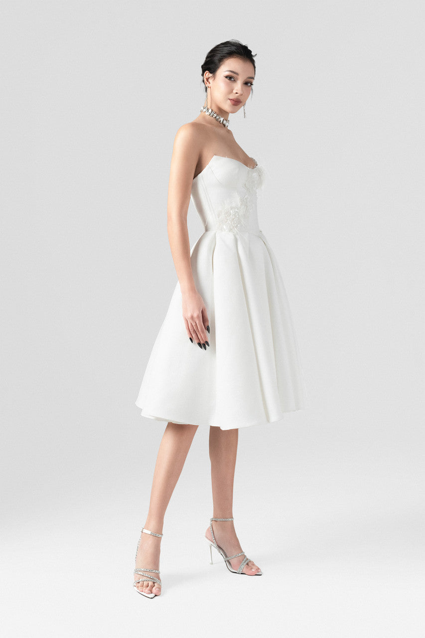 An white midi dress in taffeta, featuring a fitted corset bodice and softly flared skirt with intricate feather and floral bead appliqués.