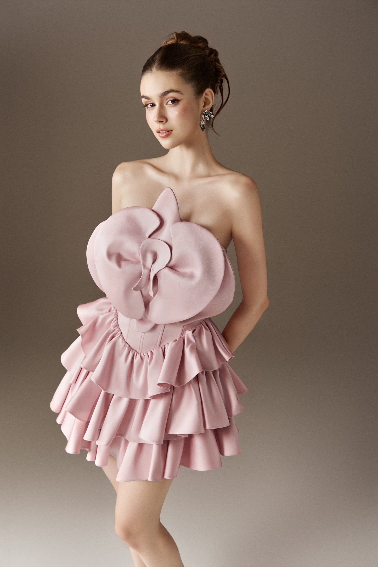 A pink strapless adult dress with a prominent 3D handmade flower bust detail and a layered ruffled skirt.