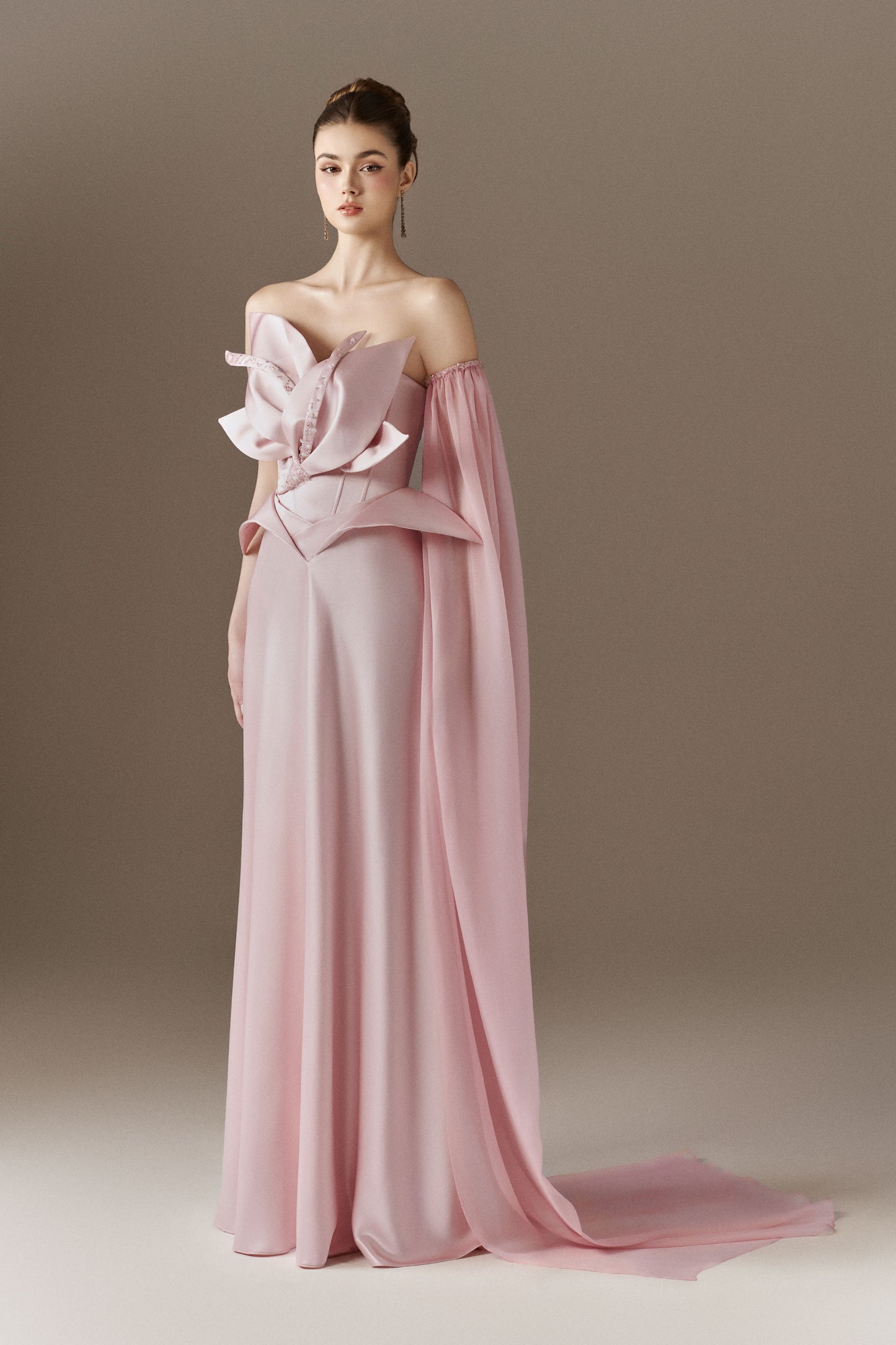 A vibrant red figure-hugging maxi dress with a bandeau neckline. The dress features a large 3D floral bust detail adorned with crystals, and a detachable single cape sleeve on the left arm.