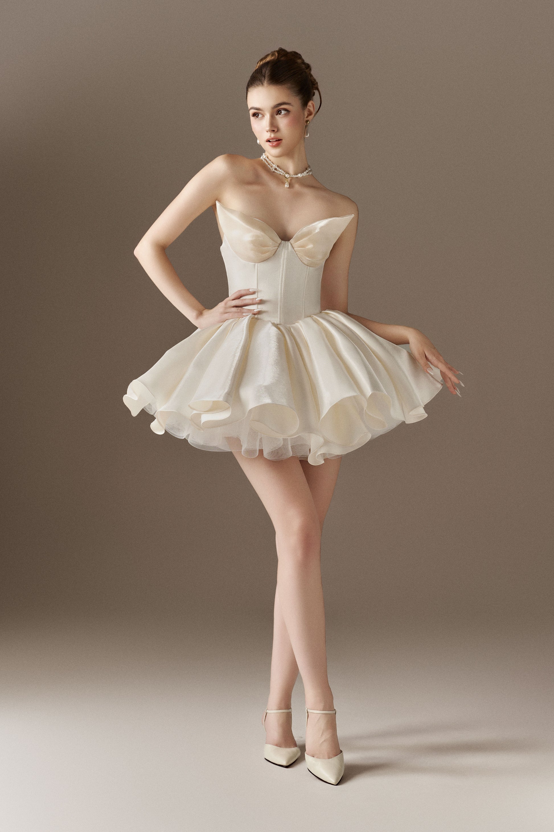 An ivory strapless mini dress with a sweetheart neckline, a corset bodice, and a voluminous puffed skirt. The skirt is accented with hand-sewn floral embellishments.