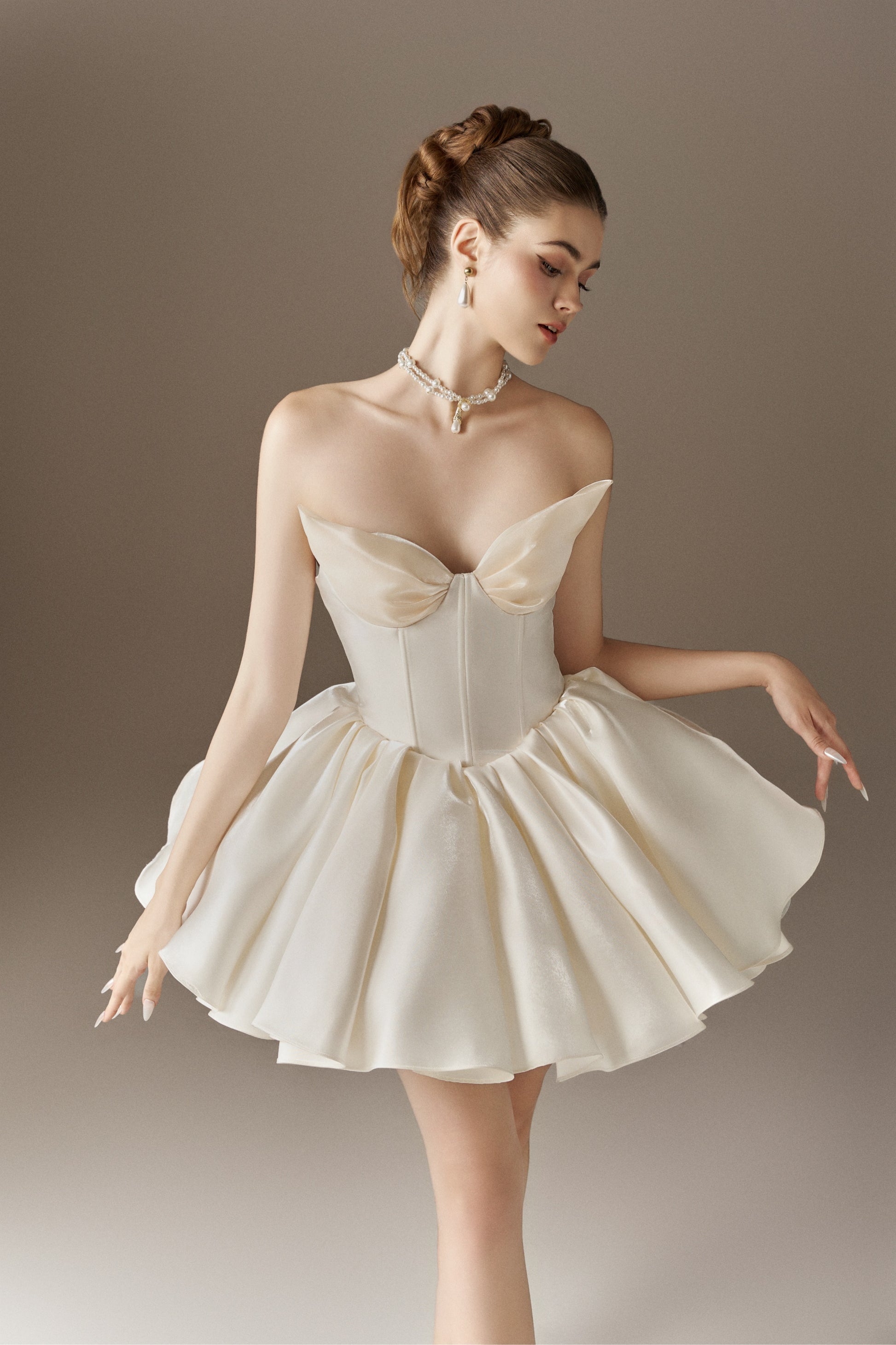 An ivory strapless mini dress with a sweetheart neckline, a corset bodice, and a voluminous puffed skirt. The skirt is adorned with hand-sewn floral embellishments.