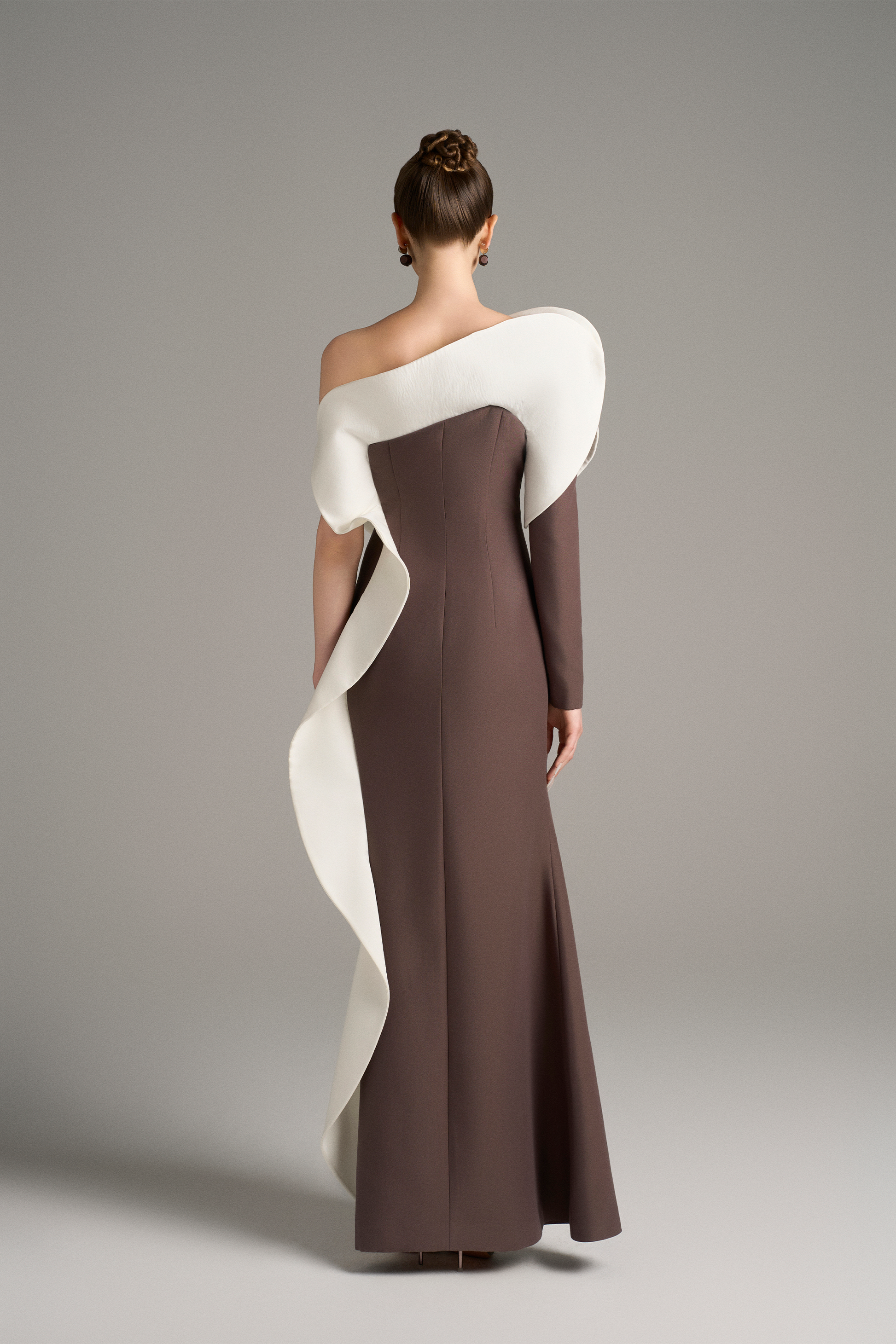 Full-body back view of the brown gown with white ruffle detail flowing from the shoulder, showing the sleek fit and long hemline.