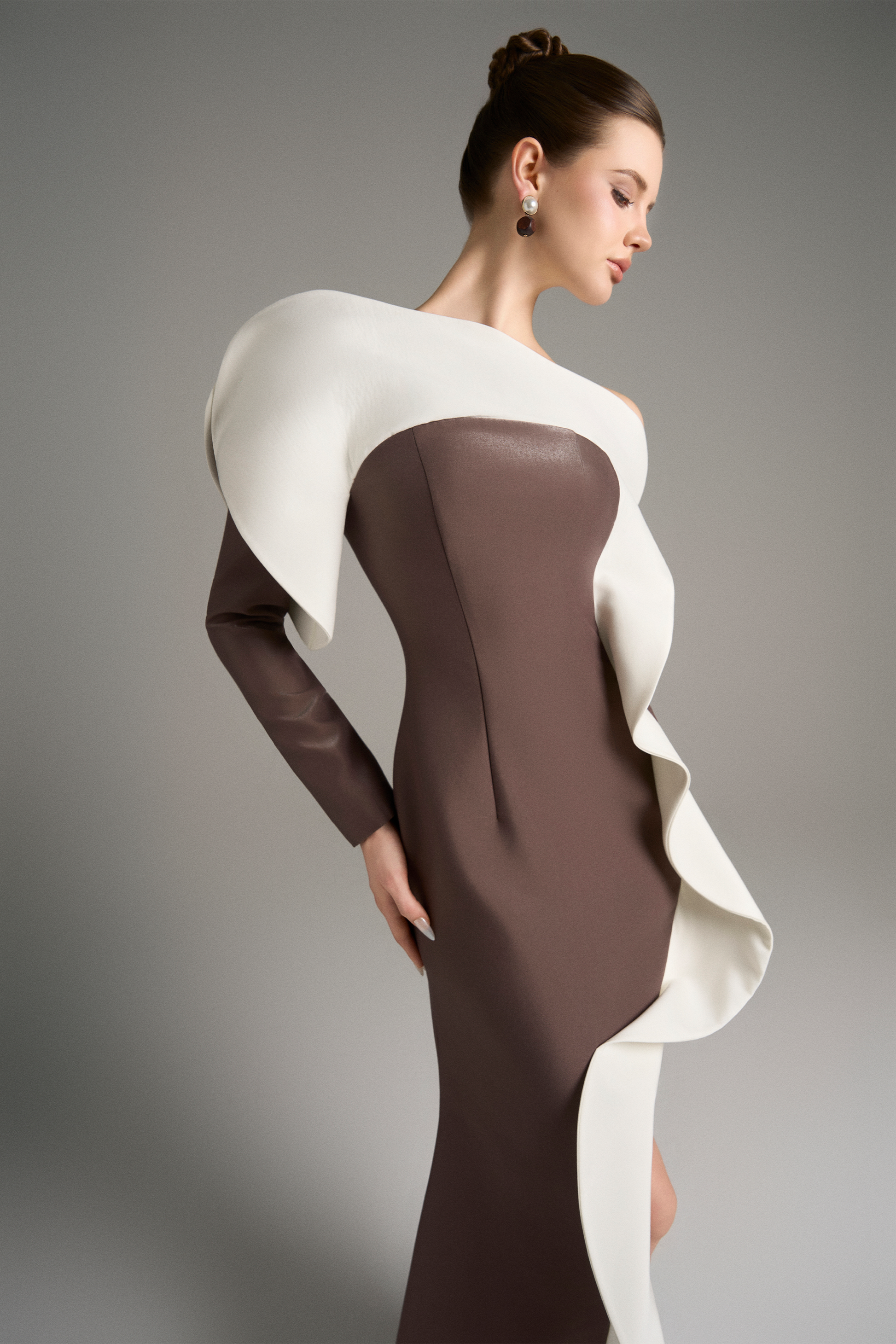 Side angle of the model in the brown gown, highlighting the voluminous white ruffle that spirals from the shoulder to the slit.