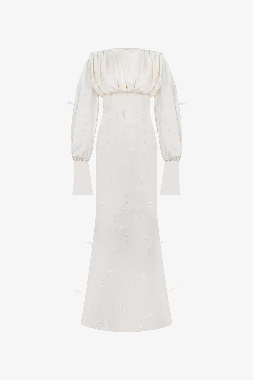 A beige silk maxi dress, adorned with intricate embellishments of feathers, pearls, and crystals. 