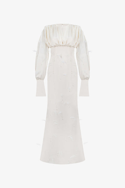A beige silk maxi dress, adorned with intricate embellishments of feathers, pearls, and crystals. 