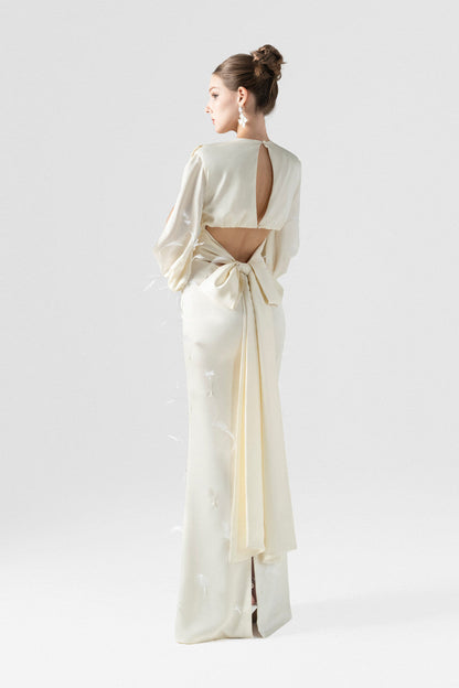 A beige silk maxi dress, adorned with intricate embellishments of feathers, pearls, and crystals. 