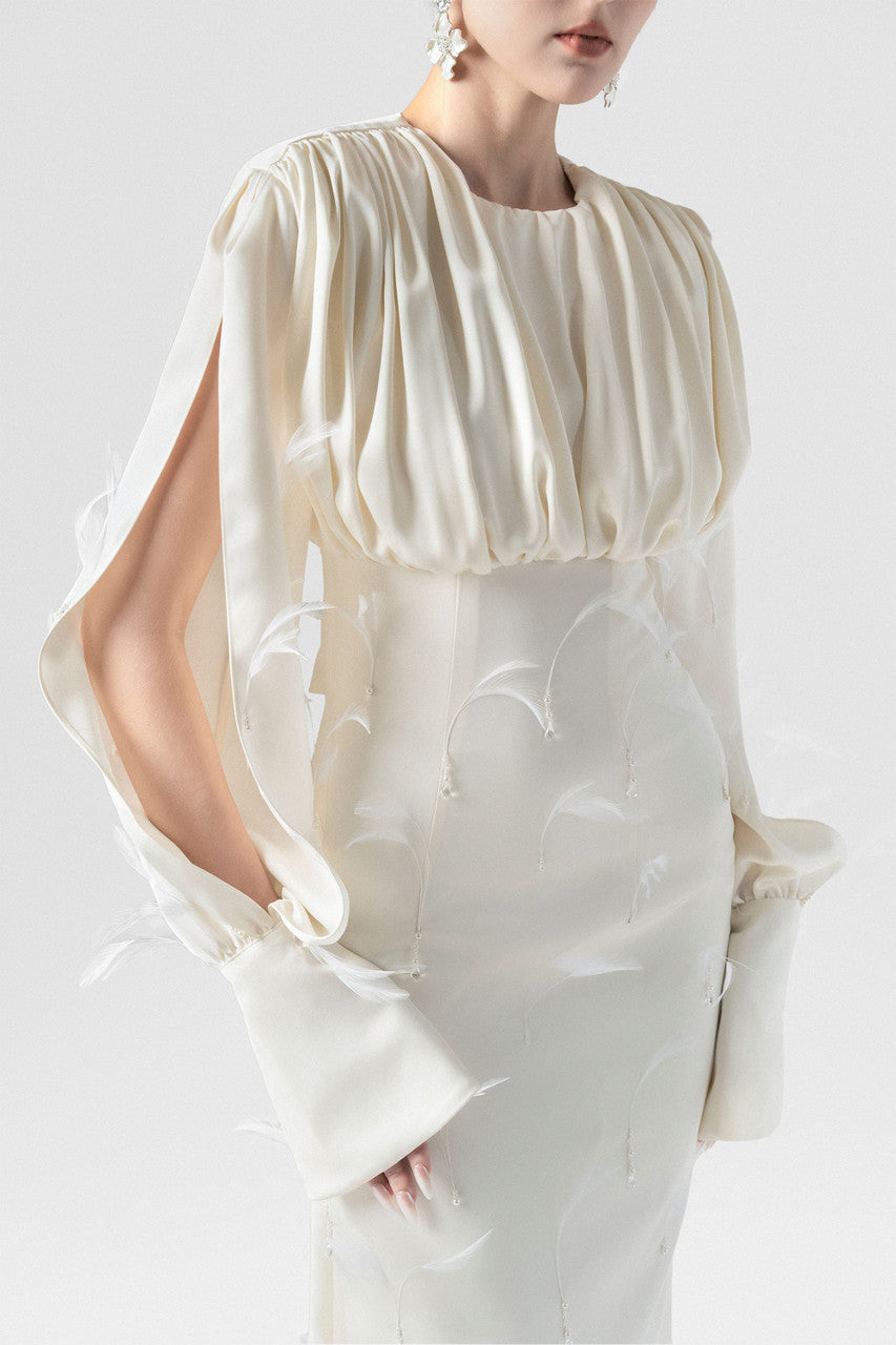 A beige silk maxi dress, adorned with intricate embellishments of feathers, pearls, and crystals. 