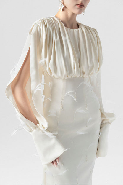 A beige silk maxi dress, adorned with intricate embellishments of feathers, pearls, and crystals. 