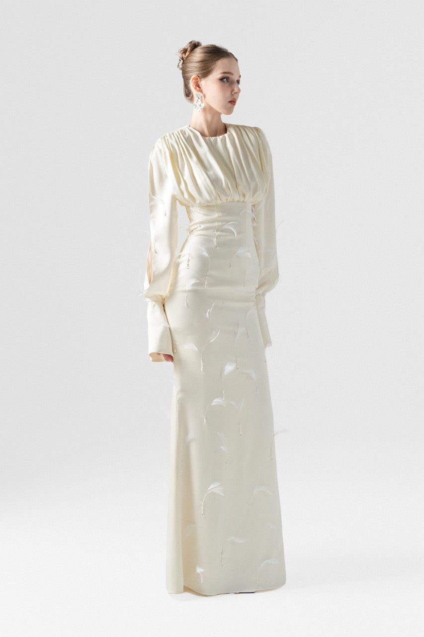 A beige silk maxi dress, adorned with intricate embellishments of feathers, pearls, and crystals. 