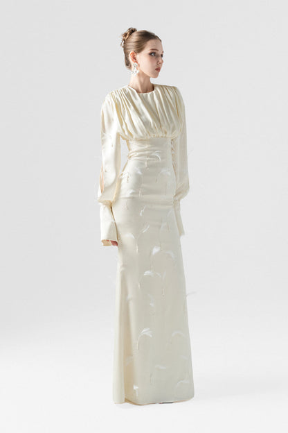 A beige silk maxi dress, adorned with intricate embellishments of feathers, pearls, and crystals. 