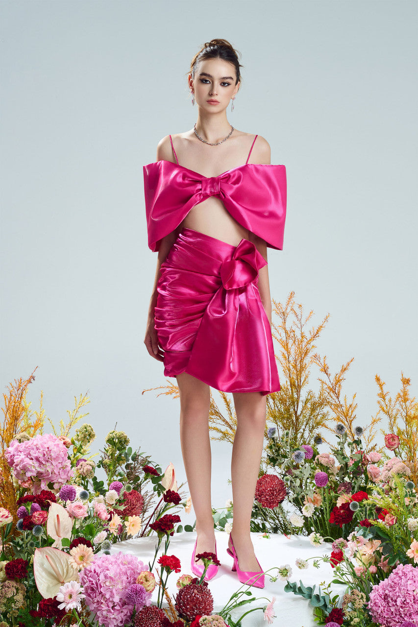 A bow-shaped crop top paired with a ruffle trim draped skirt. Available in rich red and pink.