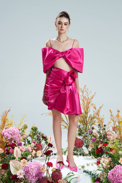 A bow-shaped crop top paired with a ruffle trim draped skirt. Available in rich red and pink.