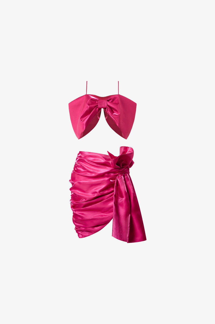 A bow-shaped crop top paired with a ruffle trim draped skirt. Available in rich red and pink.