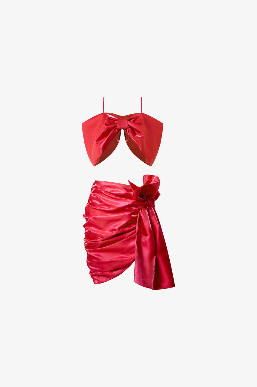 A bow-shaped crop top paired with a ruffle trim draped skirt. Available in rich red and pink.