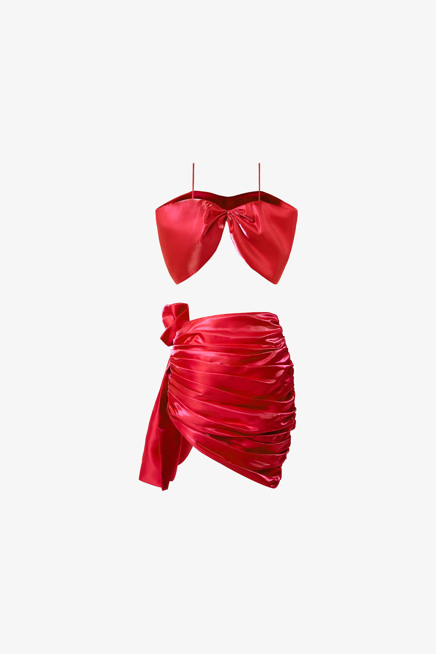 A bow-shaped crop top paired with a ruffle trim draped skirt. Available in rich red and pink.