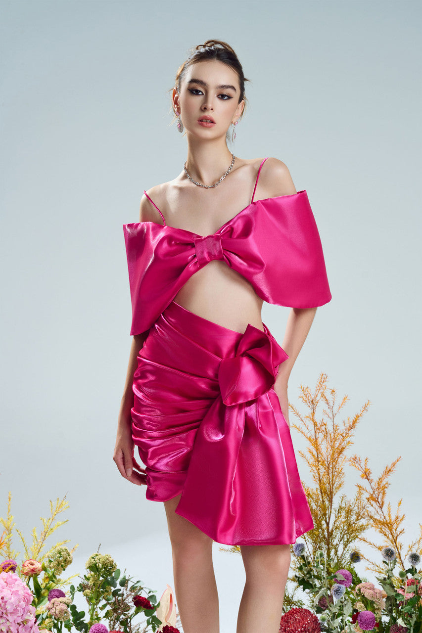 A bow-shaped crop top paired with a ruffle trim draped skirt. Available in rich red and pink.