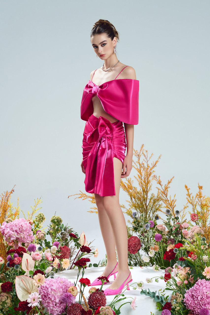 A bow-shaped crop top paired with a ruffle trim draped skirt. Available in rich red and pink.