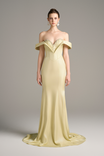 A model wearing an off-shoulder, lemon yellow silk mermaid gown with a sweetheart neckline, corset bodice, and crystal embellishments.
