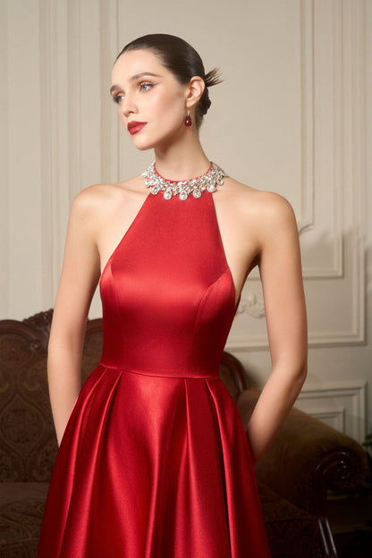 A red silk dress with a fitted halter neck bodice with intricate embellishments and a flowing, flared skirt. 