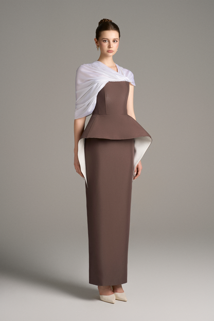 Three-quarter view of strapless column gown with structured peplum detail and draped white shoulder wrap