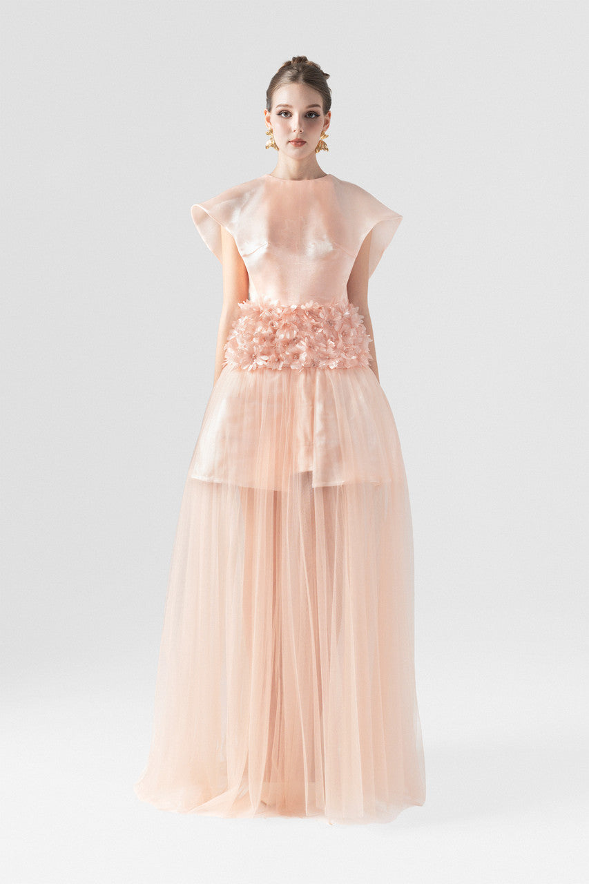 The pink maxi dress in organza, featuring wing sleeves, floral-embellished waist, and floor-length see-through ruffle hem. 