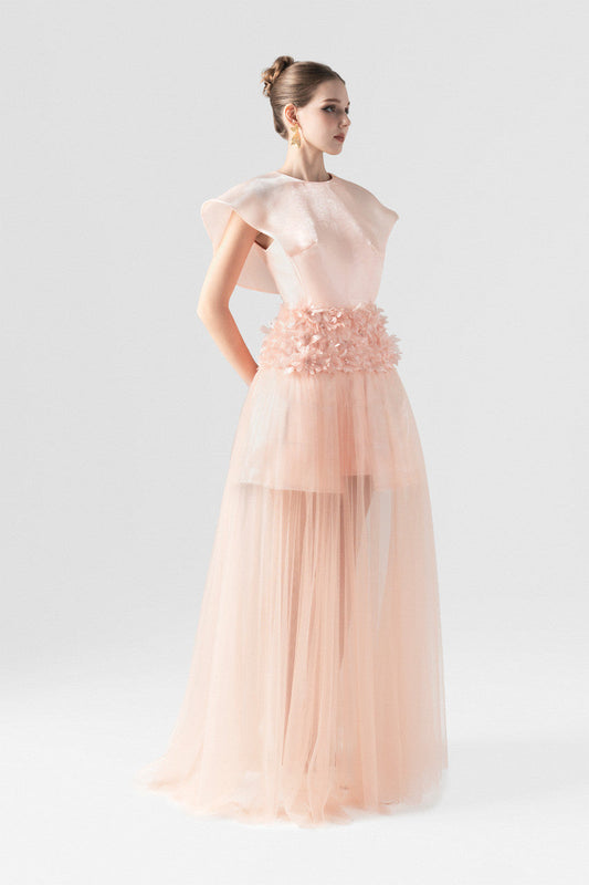 The pink maxi dress in organza, featuring wing sleeves, floral-embellished waist, and floor-length see-through ruffle hem. 